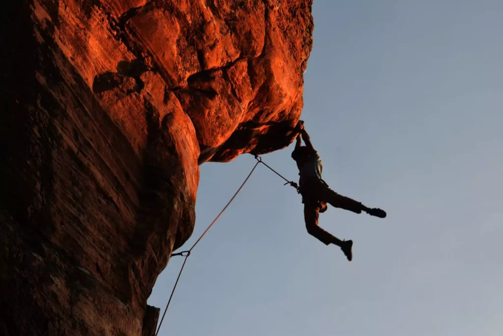a person rock climbing, suspended from the rock, praying for the impossible