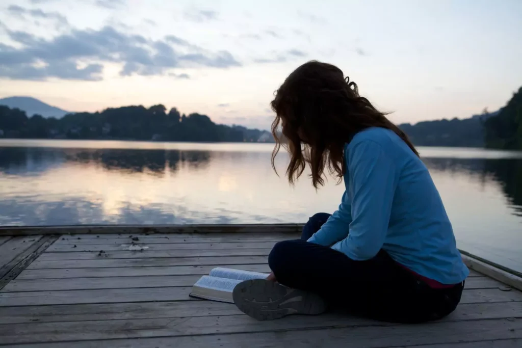 a woman reading her bible on a dock, maintaining her faith after her parents' divorce