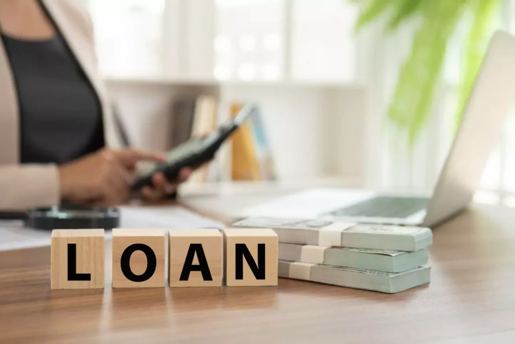 a stack of money to borrow next to blocks on a desk that spell "loan"