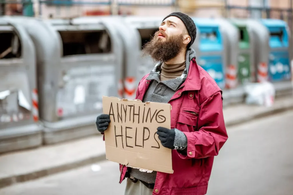 a beggar holding a sign that says "anything helps"