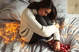 a sad woman sitting on her bed surrounded by Christmas lights, not having a perfect Christmas