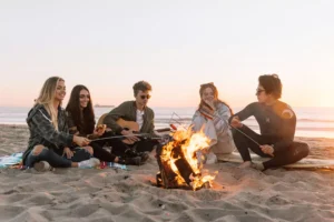 5 friends sitting around a campfire, one is trying to be a wingman for their friend