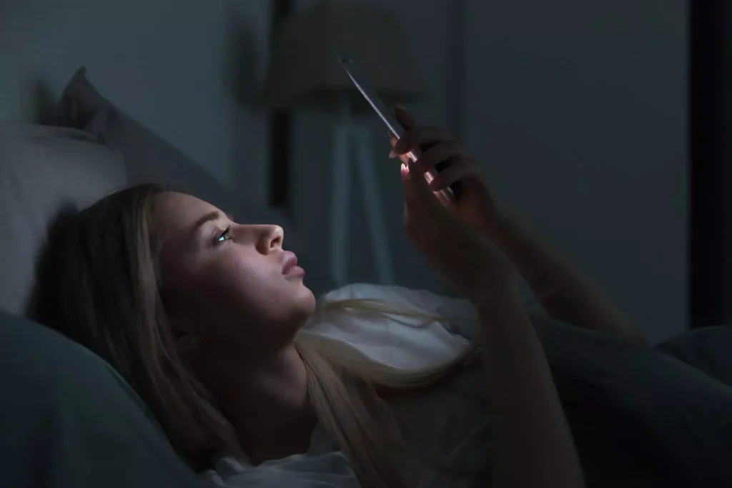 A woman lying in bed, seemingly looking at pornography on her phone