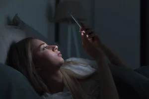 A woman lying in bed, seemingly looking at pornography on her phone