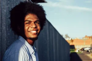 a man leaning against a fence, smiling, free from shame